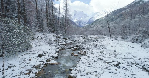 Aerial view of winter landscape in the snow mountain woods camera move above flowing stream in snowing forest with snow mountain in the background in Sichuan China Siguniangshan National Park photo