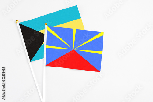 Reunion and Bahamas stick flags on white background. High quality fabric, miniature national flag. Peaceful global concept.White floor for copy space.