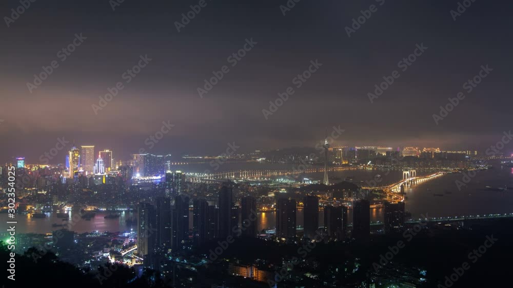 Timelapse modern buildings and skyscrapers of Macau Peninsula districts connected by large bridges reflected in water at dark cloudy night in China Timelapse modern buildings and skyscrapers of Macau Peninsula districts connected by large bridges reflected in water at dark cloudy night in China