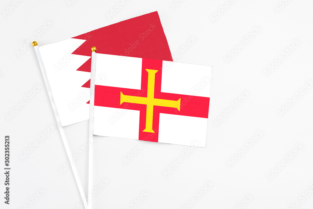 Guernsey and Bahrain stick flags on white background. High quality fabric, miniature national flag. Peaceful global concept.White floor for copy space.
