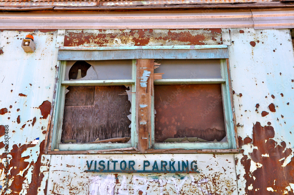 Naklejka premium Urban grunge scene of a windows and a peeling wall with a visitors parking sign attached.