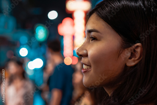 Headshot of young millennial Asian girl shopping at night market - Diverse Thai Chinese woman smiling with urban city night background - nightlife, travel and lifestyle concept with orange teal filter