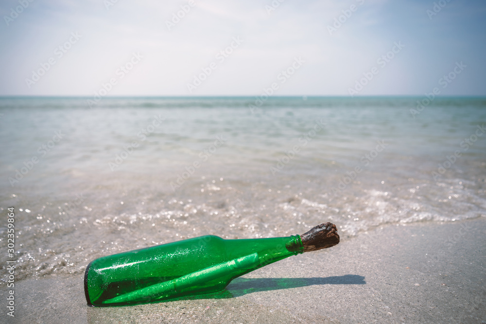 The glass bottle is closed with cork on the beach. Inside there is a paper roll. The glass bottle is closed with cork on the beach. Inside there is a paper roll.