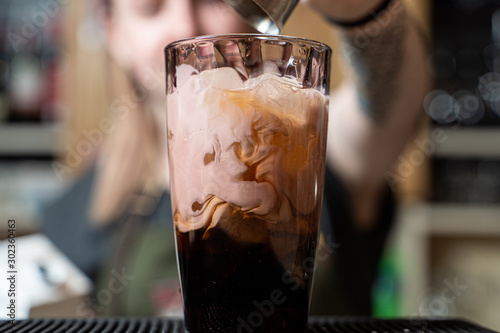 Bartender is making milky alcoholic cocktail pouring and stirring cream into the glass