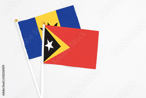 East Timor and Barbados stick flags on white background. High quality fabric, miniature national flag. Peaceful global concept.White floor for copy space.