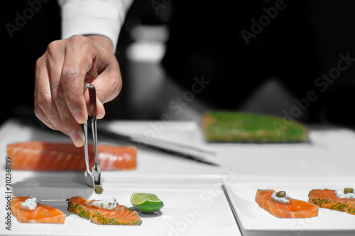 Professional chef decorating caper on sliced salmon