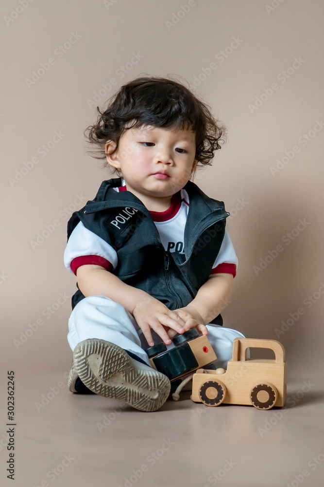 Asian kid tired after playing with so toys on light brown background. Asian kid tired after playing with so toys on light brown background.