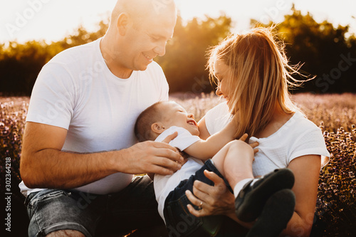 Portrait of a beautiful family embracing while playing outdoor. Mother and father embracing and playing with their little kid against sunset. photo