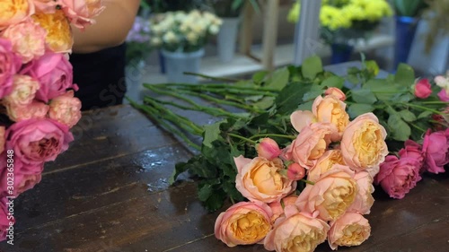 Florist woman making bouquet of pink and orange peonies in flower shop, closeup hands. Floral business concept. She creates professional bunch composition in floristic studio store at table.
