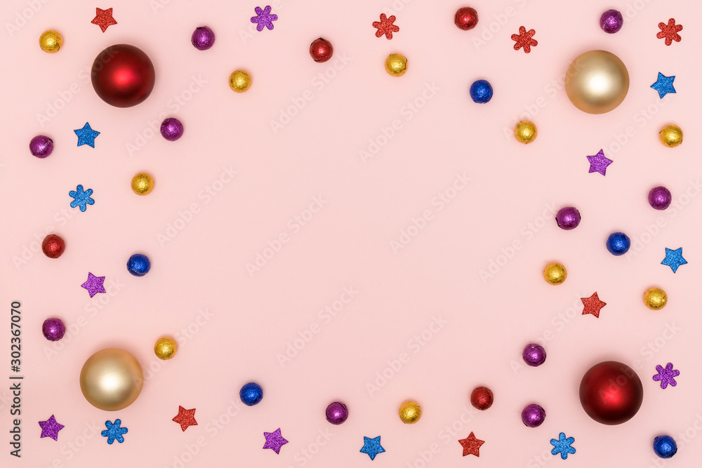 New Year and Christmas frame. Multicolored shiny christmas decorations - chocolate candies, christmas balls, decorative stars and snowflakes on pink paper background. Top view, flat lay, copy space