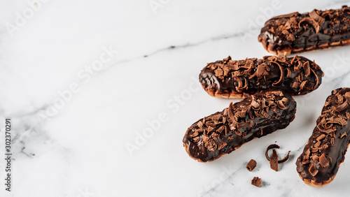 Set of homemade eclairs with chocolate on white marble background. Close up view of delicious healthy profitroles with chocolate glaze. Copy space for text or design. Banner