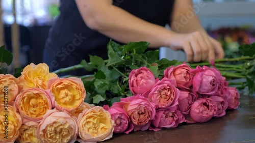 Florist woman preparing pink and orange peonies to bouquet in flower shop, hands closeup view. Floral business concept. She creates professional bunch composition in floristic studio store at table.