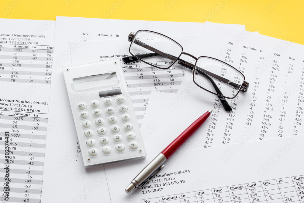 Taxes calculation concept. Financial documents, calculator, glasses on yellow background Taxes calculation concept. Financial documents, calculator, glasses on yellow background