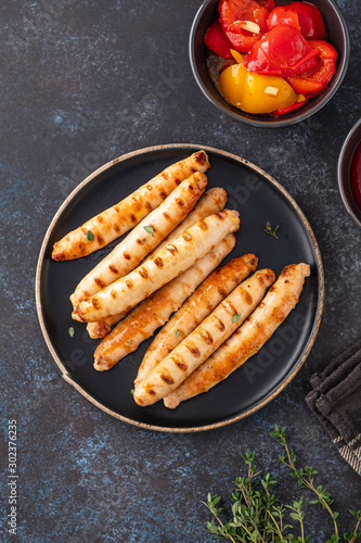 Grilled sausages on black plate with tomato sauce and thyme. Copy space.