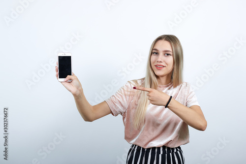 Gorgeous caucasian young woman on pretty clothes holding IPhone over isolated yellow background stay and laughing. Looks very happy pointing with hand and finger