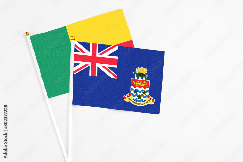 Fototapeta premium Cayman Islands and Benin stick flags on white background. High quality fabric, miniature national flag. Peaceful global concept.White floor for copy space.