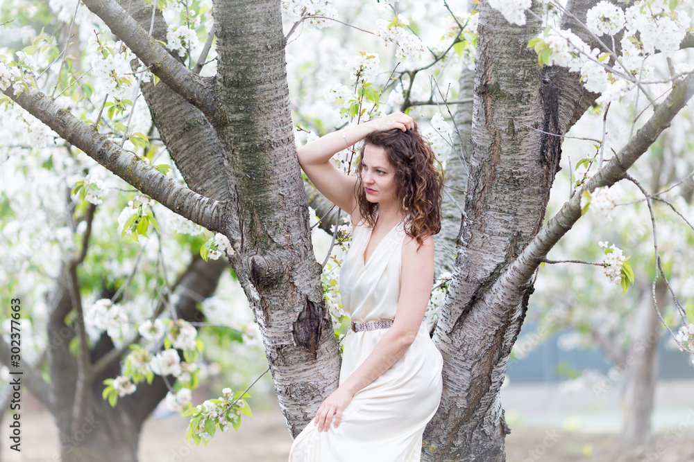 A portrait of beautiful young Caucasian woman with curly dark hair in blossoming orchard A portrait of beautiful young Caucasian woman with curly dark hair in blossoming orchard