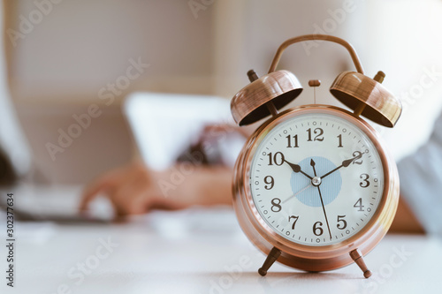 Alarm clock on white table background with businessman working with laptop.Time management and punctuality at work concept.