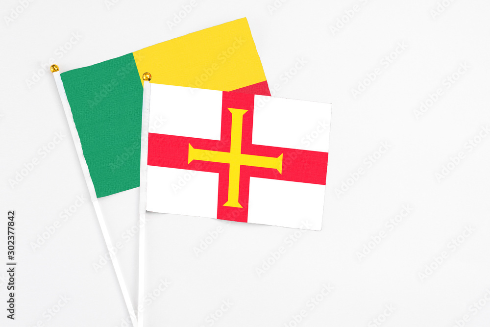 Guernsey and Benin stick flags on white background. High quality fabric, miniature national flag. Peaceful global concept.White floor for copy space.