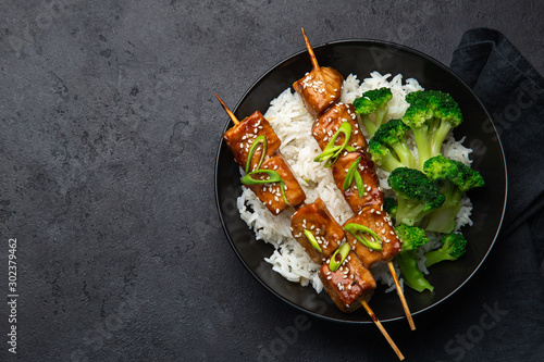 Teriyaki salmon skewers with rice and broccoli on black plate photo