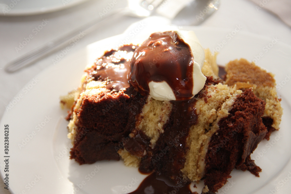 Traditional Hungarian sweet dessert with whipped cream and chocolate sauce called somloi galuska on a white plate on a set table Traditional Hungarian sweet dessert with whipped cream and chocolate sauce called somloi galuska on a white plate on a set table