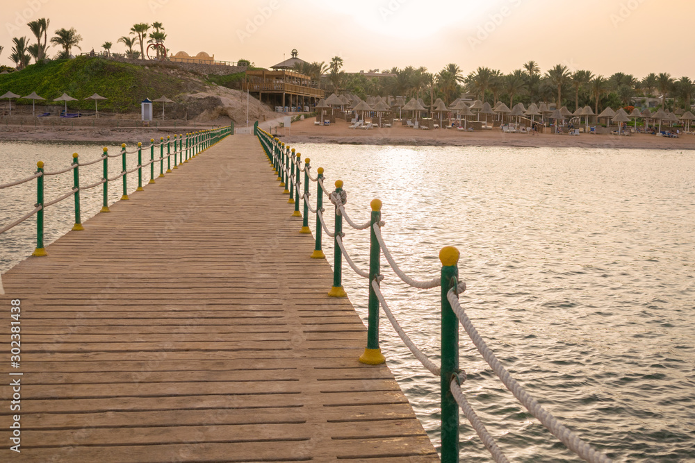 Naklejka premium A large wooden pier is on the sandy beach of the resort. Beautiful view of the tropical coast with a long pantone. Landscape of the sea coast