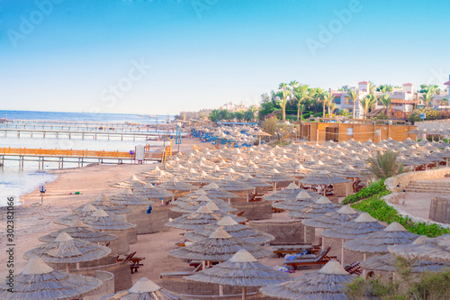  There are many of sun umbrellas and deck chairs on the beach. The coastline of a popular resort town. Beautiful landscape of the sea coast in the tropics.