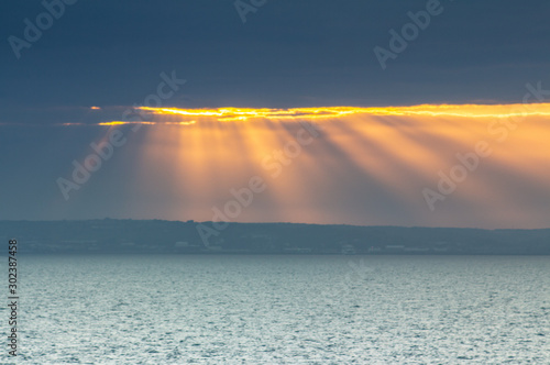 Sunligh Sun beams shining on sea surface through opening hole in thick clouds. Dramatic sunset by the coast.  photo