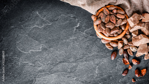 Cocoa beans on dak stone table top view. Dark chocolate and powder in wooden bowl copy space for text or banner. photo