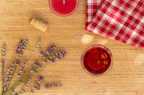 Red wine glass and candle with lavender and checked cloth on wooden table, romantic flatlay, top view 