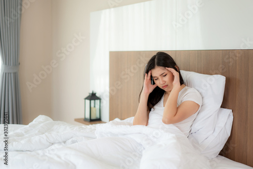 Attractive young Asian woman wake up on her bed holding their hand from headache and looking unhappy and feeling headache / migraine / stress / sick. Concept of women's health care.