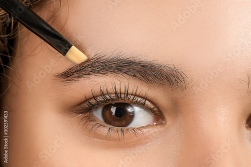 Young woman correcting shape of her eyebrows, closeup