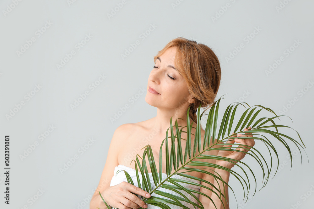 Mature woman with tropical leaf on light background Mature woman with tropical leaf on light background