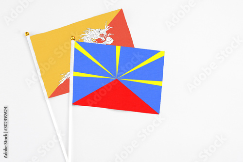 Reunion and Bhutan stick flags on white background. High quality fabric, miniature national flag. Peaceful global concept.White floor for copy space.