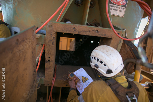 Certifies miner wearing fall body harness helmet protection holding gas test detector confined space permit book and inspecting safety environment surrounding before conduct gas testing prior entry photo