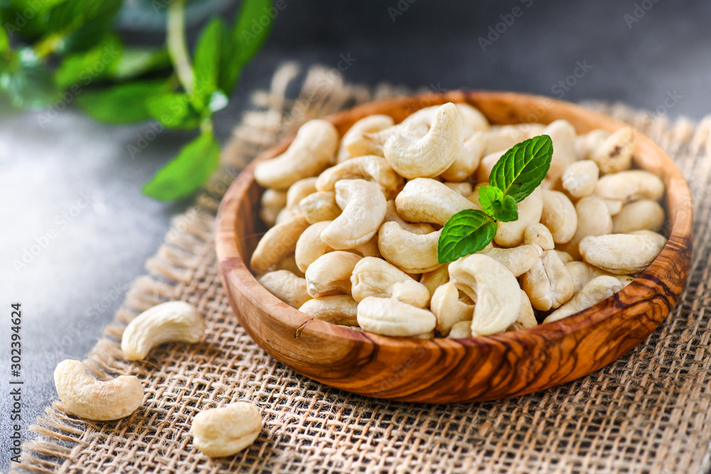 Cashew nuts in a wooden bowl on dark stone board with blurred background. Cashew nuts in a wooden bowl on dark stone board with blurred background.