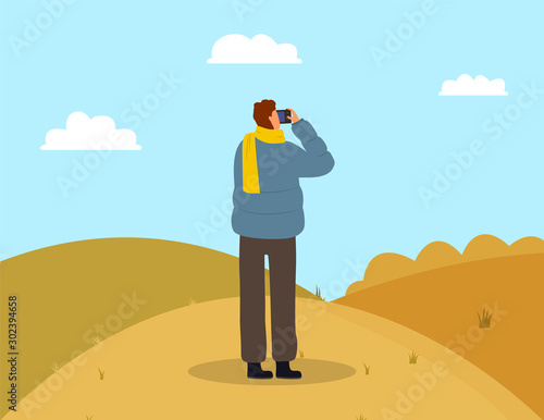 Man photographing picturesque view. Male wearing casual clothes and scarf standing on grass and making photo. Back view of person photographer holding shooting landscape of autumn park vector