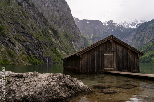 Bergsee mit Fischerhütte aus Holz an einem regnerischen wolkigen Sommertag