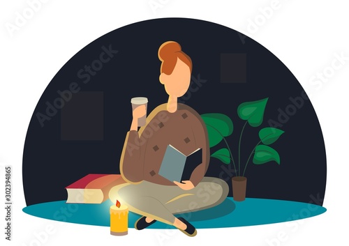 Cute lady sitting on the floor and reading book with a Cup of coffee in hand . Adorable young woman spending weekend at home. Leisure activity, repose and relaxation. Candle lights the room at night