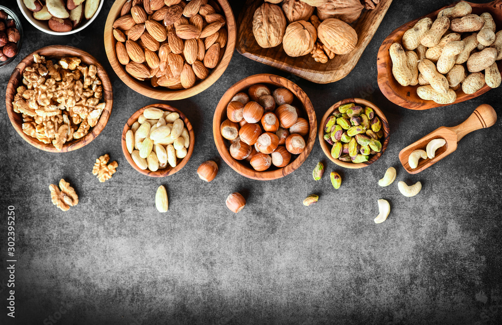 A variety of nuts in wooden bowls from top view. Walnuts, cashew, almond, pistachio, pecan, hazelnut, macadamia and peanut mix selection. Healthy fitness super food banner or panorama. A variety of nuts in wooden bowls from top view. Walnuts, cashew, almond, pistachio, pecan, hazelnut, macadamia and peanut mix selection. Healthy fitness super food banner or panorama.