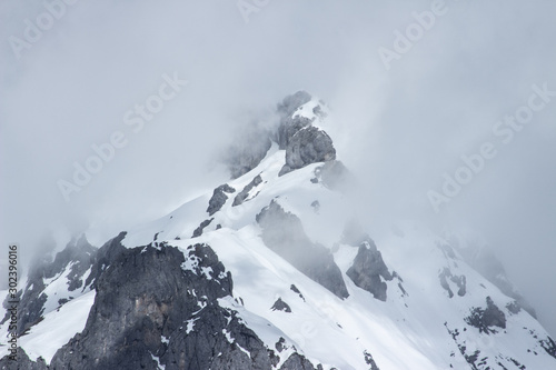 Top of snow mountain in cloud, fog on rocky ridge photo