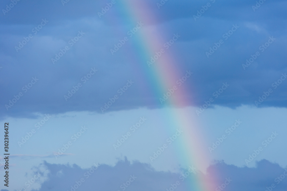A piece of rainbow in the sky against the background of rain clouds.