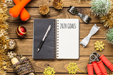 New year 2020 goals for healthy lifestyle, lose weight and join gym concept. 2020 Goals written in notebook with dumbbells, jump ropes and Christmas ornaments decorations.