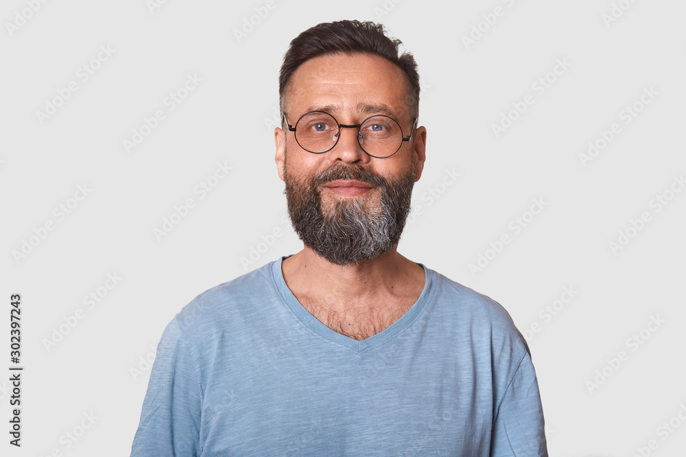 Close up portrait of handsome middle aged bearded Caucasian man with smile, male wearing gray casual t shirt, posing isolated over white background, looking directly at camera, looks satisfied.