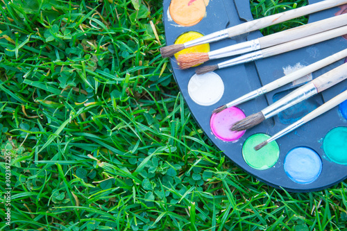 Watercolor paints and tassels of different sizes. Paints and brushes lie on green grass. The heyday of nature. The beginning of a new life. Art.