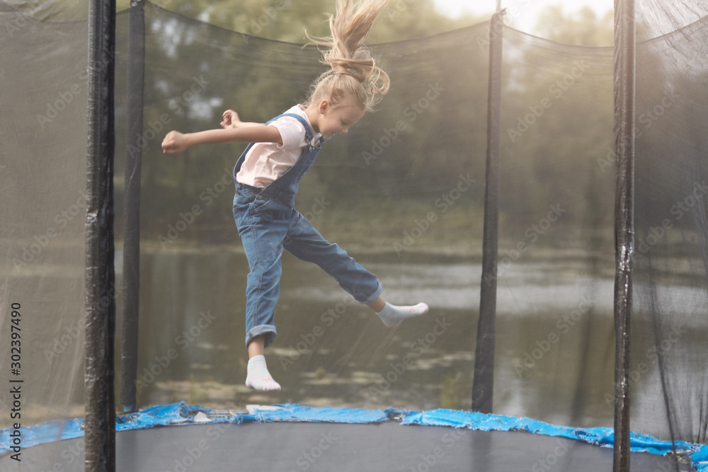 Full length photo of happy girl jumping high on trampoline in park, blonde  female chicd with