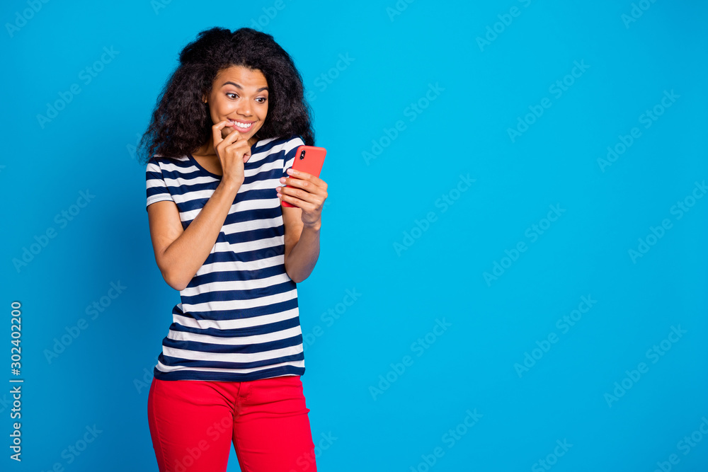 Photo of cheerful positive nice pretty youngster browsing through phone having received new sms rejoicing her smiling toothily biting nails near empty space isolated blue vivid color background Photo of cheerful positive nice pretty youngster browsing through phone having received new sms rejoicing her smiling toothily biting nails near empty space isolated blue vivid color background
