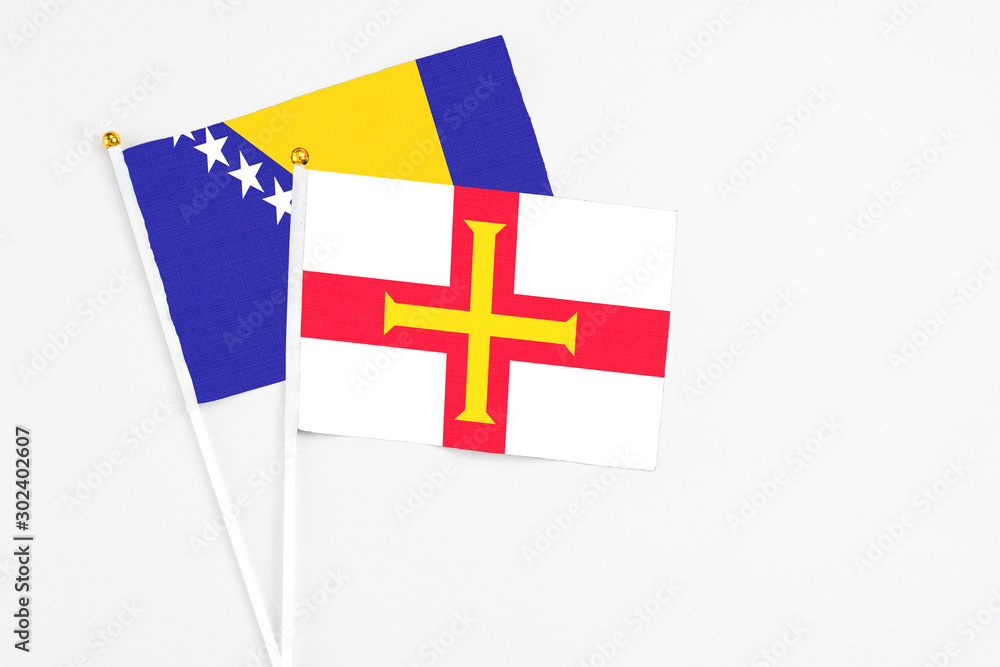 Guernsey and Bosnia Herzegovina stick flags on white background. High quality fabric, miniature national flag. Peaceful global concept.White floor for copy space.