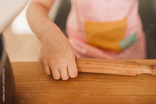 children's hand holds a rolling pin on a wooden table