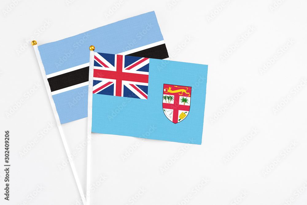 Fototapeta premium Fiji and Botswana stick flags on white background. High quality fabric, miniature national flag. Peaceful global concept.White floor for copy space.
